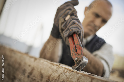 Foto: A man working in a reclaimed timber yard. Using a tool to remove metals from a reclaimed piece of timber. A man working in a reclaimed timber yard. Using a tool to remove metals from a reclaimed piece of timber.