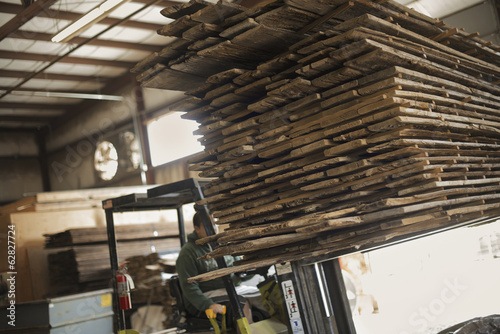 Foto: A heap of recycled reclaimed timber planks of wood being moved on a forklift truck. Environmentally responsible reclamation in a timber yard. A heap of recycled reclaimed timber planks of wood being moved on a forklift truck. Environmentally responsible reclamation in a timber yard.