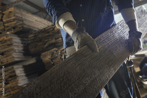 Foto: A heap of recycled reclaimed timber planks of wood. Environmentally responsible reclamation in a timber yard. A man carrying a large plank of wood. A heap of recycled reclaimed timber planks of wood. Environmentally responsible reclamation in a timber yard. A man carrying a large plank of wood.