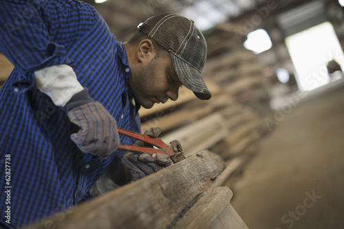 Foto: A man working in a reclaimed timber yard. Using a tool to remove metals from a reclaimed piece of timber. Workshop. A man working in a reclaimed timber yard. Using a tool to remove metals from a reclaimed piece of timber. Workshop.