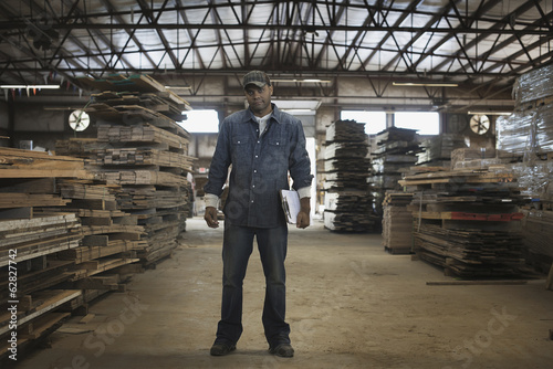 Foto: A heap of recycled reclaimed timber planks of wood. Environmentally responsible reclamation in a timber yard. A man in work overalls with a clipboard. A heap of recycled reclaimed timber planks of wood. Environmentally responsible reclamation in a timber yard. A man in work overalls with a clipboard.