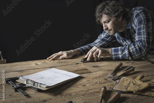 Foto: A man working in a reclaimed lumber yard workshop. Holding tools and sanding knotted and uneven piece of wood. A man working in a reclaimed lumber yard workshop. Holding tools and sanding knotted and uneven piece of wood.