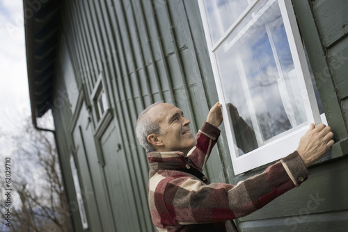 Photo: An organic farm in winter. Maintenance. A man holding a a storm window panel against the window frame. An organic farm in winter. Maintenance. A man holding a a storm window panel against the window frame.
