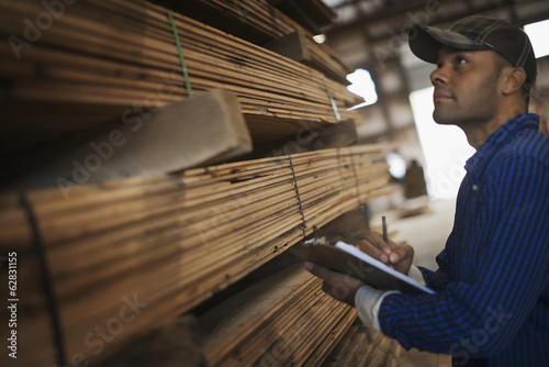 Foto: A heap of recycled reclaimed timber planks of wood. Environmentally responsible reclamation in a timber yard. A man with a clipboard by a rack of planks. A heap of recycled reclaimed timber planks of wood. Environmentally responsible reclamation in a timber yard. A man with a clipboard by a rack of planks.