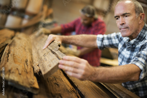 Foto: A reclaimed lumber workshop. A group of people working. A man measuring and checking planks of wood for re-use and recycling. A reclaimed lumber workshop. A group of people working. A man measuring and checking planks of wood for re-use and recycling.
