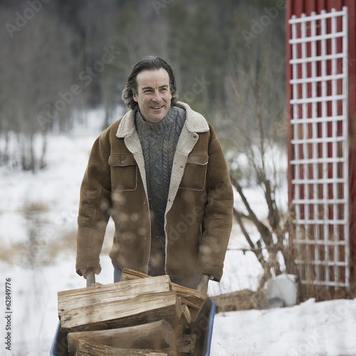 Photo: An organic farm in winter in New York State, USA. A man wheeling a barrow of firewood. An organic farm in winter in New York State, USA. A man wheeling a barrow of firewood.