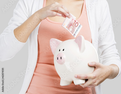 Photo: Beautiful woman putting money in a piggy bank Beautiful woman putting money in a piggy bank