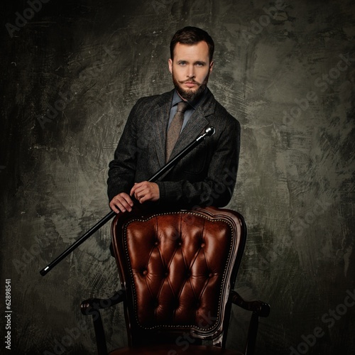 Photo: Handsome well-dressed man with stick near chair Handsome well-dressed man with stick near chair
