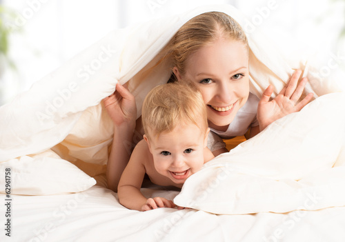 Photo: happy family mother and baby under blankets in bed happy family mother and baby under blankets in bed
