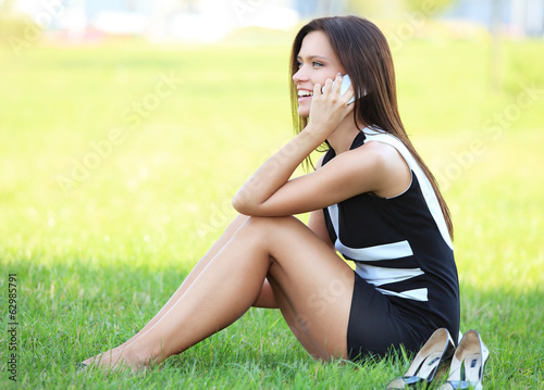 Photo: young beautiful smiling business woman sitting on the grass. young beautiful smiling business woman sitting on the grass.