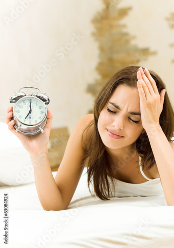 Photo: Woman with alarmclock on the bed Woman with alarmclock on the bed