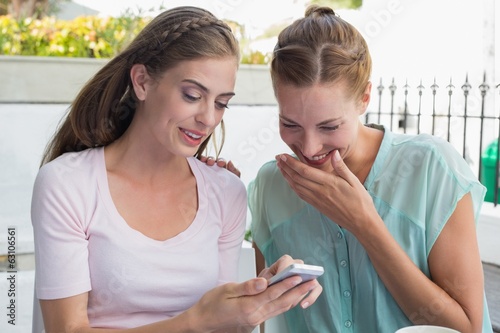 Photo: Happy female friends reading text message at coffee shop Happy female friends reading text message at coffee shop