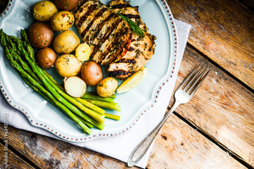 Photo: Grilled chicken with potatoes and asparagus on wooden background Grilled chicken with potatoes and asparagus on wooden background