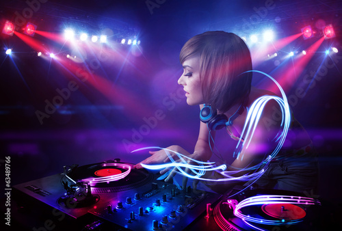 Photo: Disc jockey girl playing music with light beam effects on stage Disc jockey girl playing music with light beam effects on stage