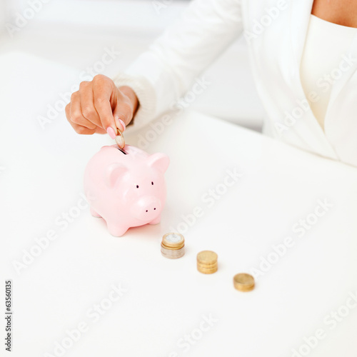 Photo: female hand putting euro coins into piggy bank female hand putting euro coins into piggy bank