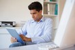 Casual businessman using his tablet at his desk Casual businessman using his tablet at his desk