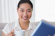 Smiling woman sitting on couch using tablet pc having coffee Smiling woman sitting on couch using tablet pc having coffee