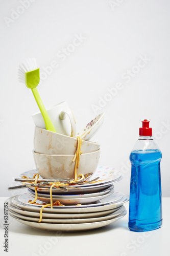 Photo: Dirty dishes pile needing washing up on white background Dirty dishes pile needing washing up on white background