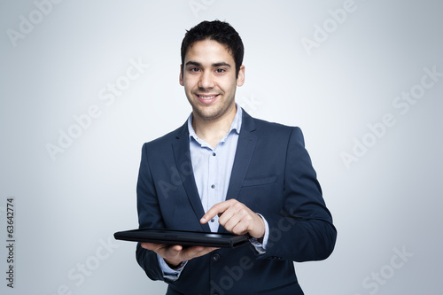 Photo: Smiling businessman working on a digital tablet against grey bac Smiling businessman working on a digital tablet against grey bac