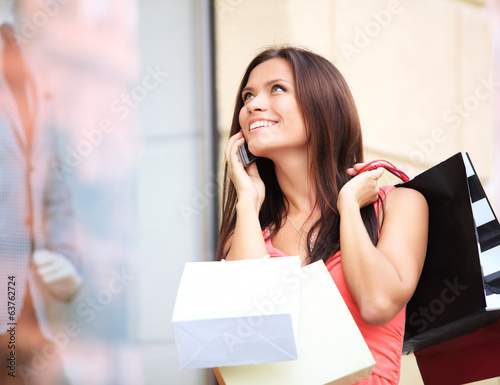 Photo: Happy woman holding shopping bags and using cell phone Happy woman holding shopping bags and using cell phone
