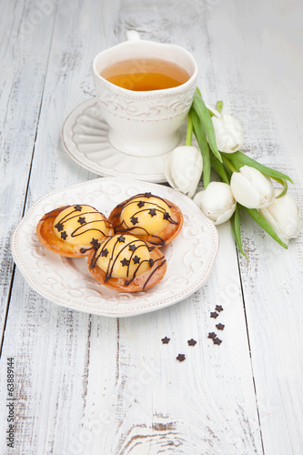 Photo: Sweet cake with cup of tea and flowers on white wooden table Sweet cake with cup of tea and flowers on white wooden table