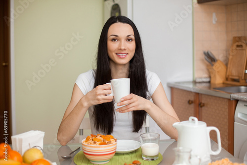 Photo: brunette girl drinking tea in the moring in the kitchen brunette girl drinking tea in the moring in the kitchen