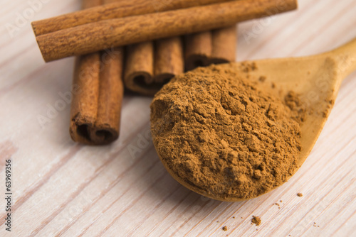 Photo: Cinnamon, whole sticks behind wooden spoon with a heap of powder Cinnamon, whole sticks behind wooden spoon with a heap of powder
