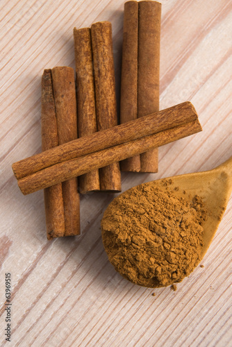 Photo: Cinnamon, whole sticks behind wooden spoon with a heap of powder Cinnamon, whole sticks behind wooden spoon with a heap of powder