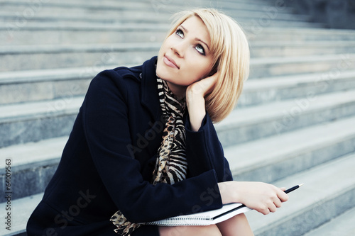 Photo: Young business woman with notebook sitting on the steps Young business woman with notebook sitting on the steps
