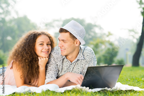 Photo: couple lying together in a park with laptop couple lying together in a park with laptop