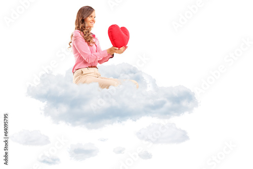 Photo: Woman holding a red heart seated in cloud Woman holding a red heart seated in cloud
