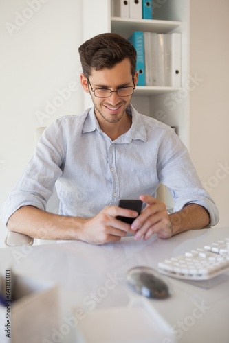Photo: Casual businessman sending a text at his desk Casual businessman sending a text at his desk