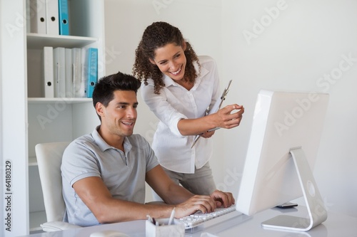 Photo: Casual business team looking at computer together at desk Casual business team looking at computer together at desk