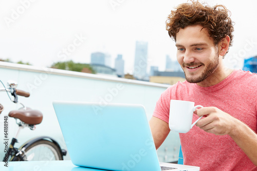 Photo: Young Man Sitting On Roof Terrace Using Laptop Young Man Sitting On Roof Terrace Using Laptop
