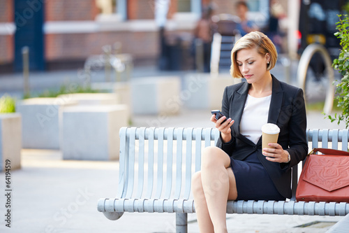 Photo: Businesswoman On Park Bench With Coffee Using Mobile Phone Businesswoman On Park Bench With Coffee Using Mobile Phone