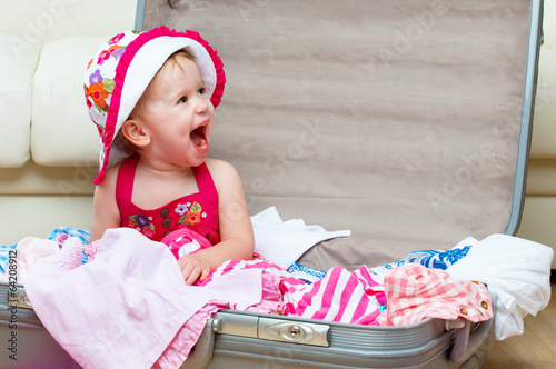 Photo: happy baby girl is going on trip, pack suitcase happy baby girl is going on trip, pack suitcase
