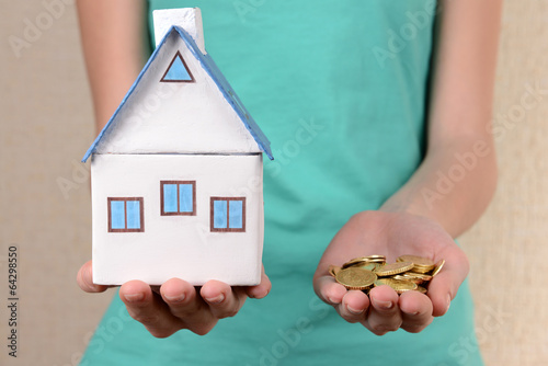 Photo: Little house-toy and coins in woman hands close-up Little house-toy and coins in woman hands close-up