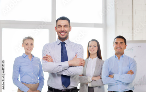 Photo: smiling businessman in office with team on back smiling businessman in office with team on back