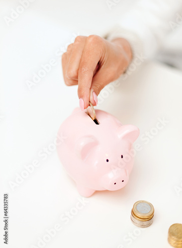 Photo: female hand putting euro coins into piggy bank female hand putting euro coins into piggy bank