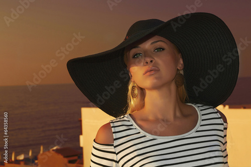 Photo: Beautiful blond woman in hat.Sunset.roof.sea.Summer Beautiful blond woman in hat.Sunset.roof.sea.Summer