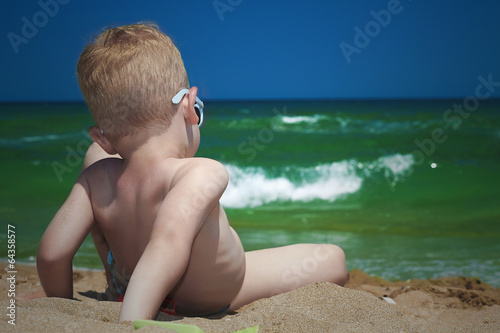 Photo: Little boy on the beach. child sitting in sand.Summer.sea.sky Little boy on the beach. child sitting in sand.Summer.sea.sky