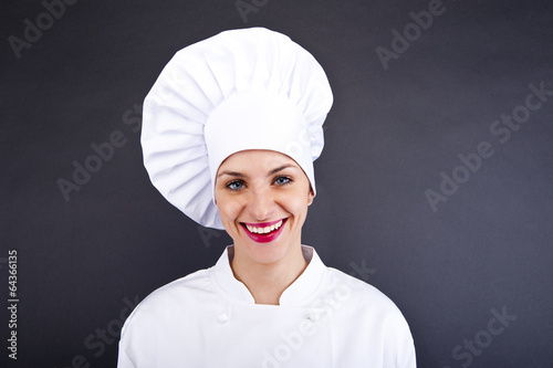 Photo: Close-up woman cook lsmiling over dark wall Close-up woman cook lsmiling over dark wall