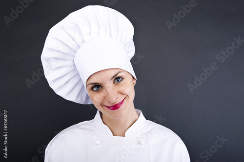 Photo: Close-up woman cook lsmiling over dark wall Close-up woman cook lsmiling over dark wall