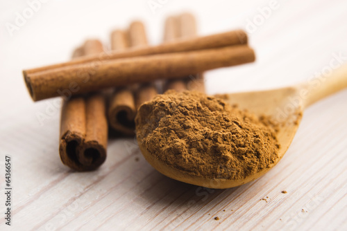 Photo: Cinnamon, whole sticks behind wooden spoon with a heap of powder Cinnamon, whole sticks behind wooden spoon with a heap of powder