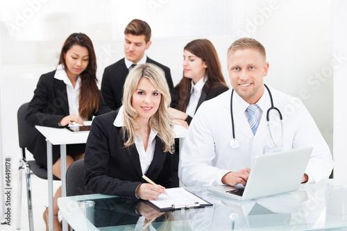 Photo: Smiling Male Doctor And Businesswoman With Laptop Smiling Male Doctor And Businesswoman With Laptop
