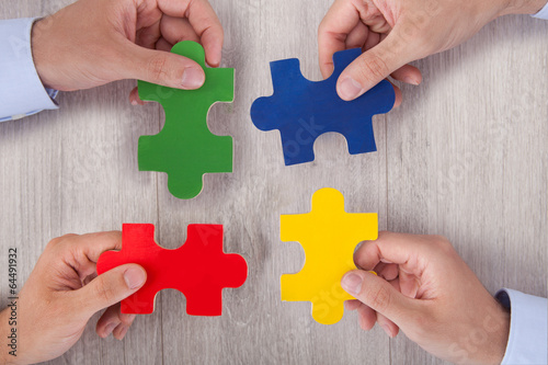 Photo: Businesspeople Joining Multicolored Puzzle Pieces At Desk Businesspeople Joining Multicolored Puzzle Pieces At Desk