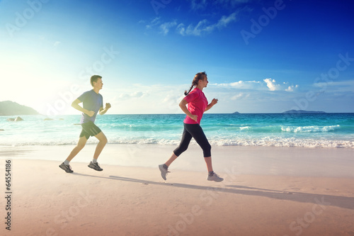 Photo: Man and women running on tropical beach at sunset Man and women running on tropical beach at sunset