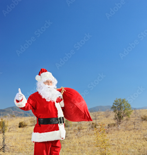 Photo: Santa holding a bag of presents and hitchhiking Santa holding a bag of presents and hitchhiking