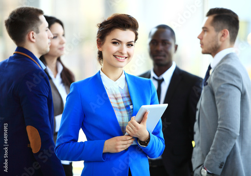 Photo: Successful business woman standing with her staff in background Successful business woman standing with her staff in background