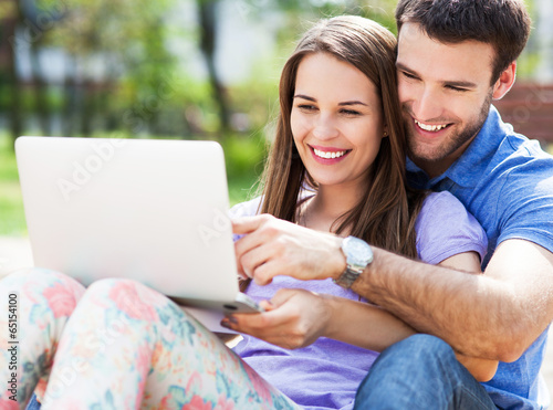 Photo: Young couple using laptop outdoors Young couple using laptop outdoors